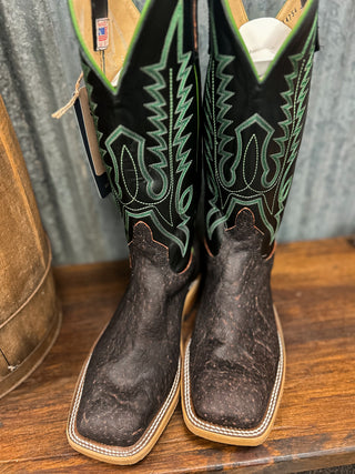Pair of black cowboy boots with green stitching on a wooden surface.