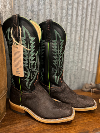 Pair of brown cowboy boots with green stitching on a wooden surface.