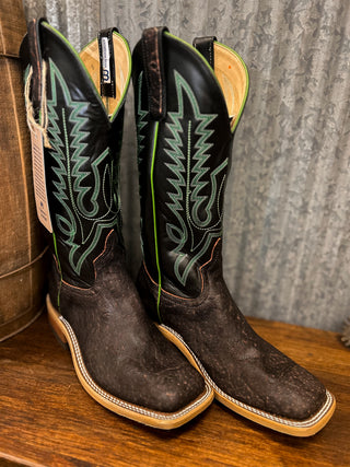 Pair of brown cowboy boots with green stitching on a wooden surface.
