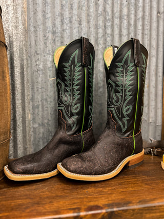 Pair of cowboy boots with intricate designs on a wooden surface and metal wall background