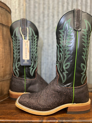 Pair of brown cowboy boots with green stitching on a wooden surface.