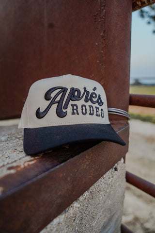Trucker hat with 'Apres Rodeo' text on a rusted metal surface