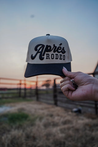 Cap with 'Apres Rodeo' text held by a hand against a sunset background.