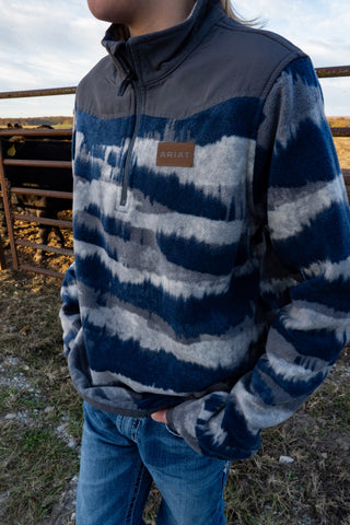 Person wearing a blue and gray striped fleece jacket with Ariat logo outdoors.