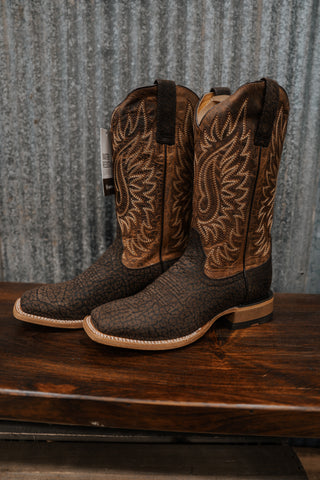Pair of brown cowboy boots with intricate patterns on a wooden surface and metal background