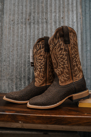 Pair of brown cowboy boots with intricate patterns on a wooden surface and metal background