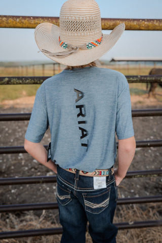 Person wearing a blue shirt with 'Ariat' branding and a straw hat, standing in front of a metal fence.