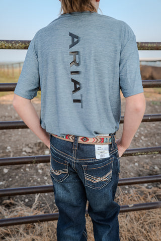 Person wearing a gray t-shirt with 'Ariat' branding, standing outdoors near a fence.