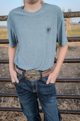 Person wearing a blue t-shirt with a logo and jeans standing in front of a metal fence.