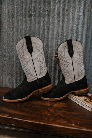 Pair of black and white cowboy boots on a wooden surface with a metal wall background