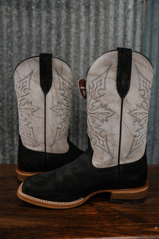 Pair of black and white cowboy boots with intricate designs on a wooden surface.