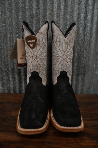 Pair of black and white Ariat cowboy boots on a wooden surface with a metal wall background.