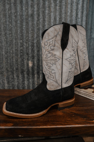 Pair of black and white cowboy boots on a wooden surface with a rustic background.