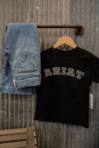 Black t-shirt with 'RHYT' text and blue jeans hanging on a wooden rack against a metal wall.