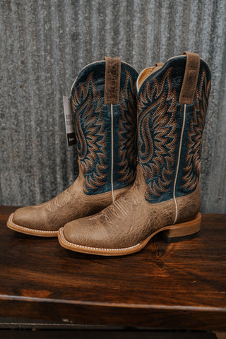 Pair of brown cowboy boots with intricate designs on a wooden surface and metal background