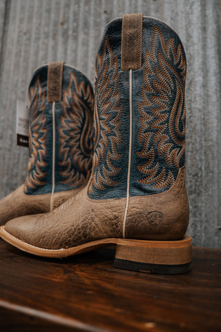 Pair of brown cowboy boots with intricate designs on a wooden surface and gray background
