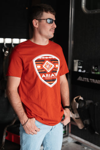 Man wearing a red Ariat t-shirt in an indoor setting with equipment in the background