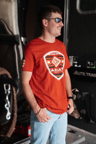 Man wearing an orange t-shirt with a logo, standing inside a vehicle.