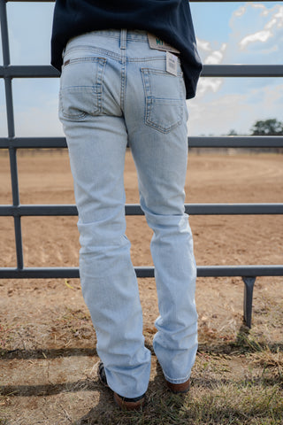 Person wearing light blue jeans standing in a fenced area with a clear sky.