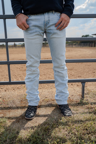 Person wearing light blue jeans standing in front of a metal fence with a rural landscape in the background.