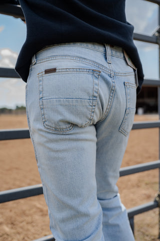 Light blue jeans worn by a person standing in front of a metal gate with a blurred background.