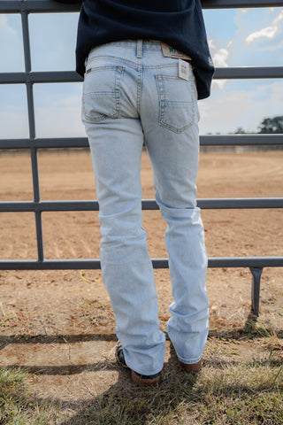 Person wearing light blue jeans standing in front of a metal fence with a field and sky in the background.