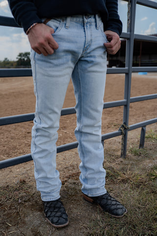 Person wearing light blue jeans standing near a metal fence in an outdoor setting.