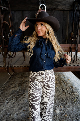 Woman wearing a cowboy hat, denim shirt, and zebra print pants in an outdoor setting.