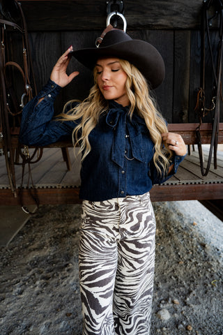 Woman wearing a cowboy hat, denim shirt, and zebra print pants in an outdoor setting.