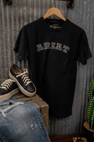 Black t-shirt with 'ABIE' design on a wooden hanger against a corrugated metal wall.
