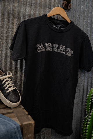 Black t-shirt with white text on a wooden hanger against a rustic metal wall.