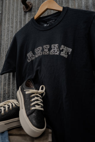 Black t-shirt with 'REBEL' print on a hanger with sneakers below.