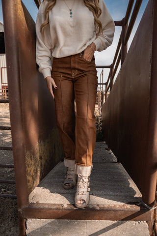 Person wearing a beige sweater and brown pants standing on a rusted metal staircase.