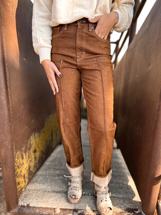 Person wearing brown high-waisted jeans and a white top standing between two large metal pipes.