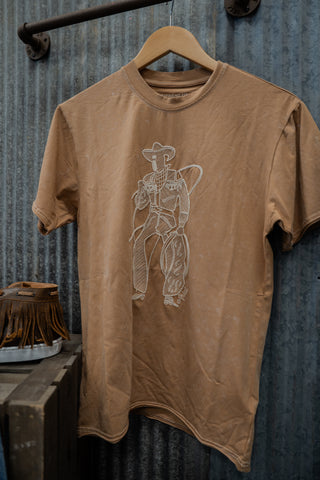 Brown t-shirt with a cowboy graphic on a hanger against a rustic metal wall.
