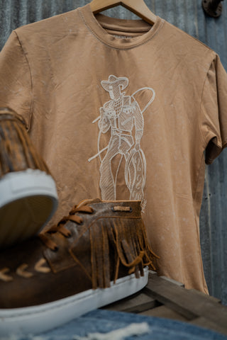 Brown t-shirt with a cowboy graphic and brown shoes on a wooden surface