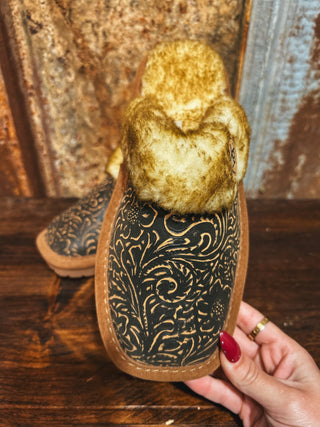 Brown slipper with intricate black patterns held by a hand on a wooden surface.
