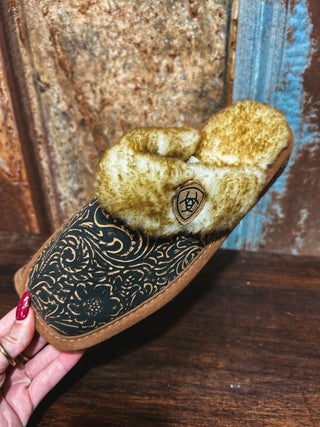 Brown slipper with patterned sole held by a hand against a rustic wooden background