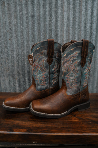 Pair of brown cowboy boots with intricate designs on a wooden surface and metal background