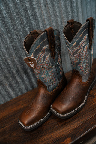Pair of brown cowboy boots with intricate designs on a wooden surface and metal background