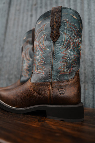 Pair of brown cowboy boots with intricate designs on a wooden surface and rustic background