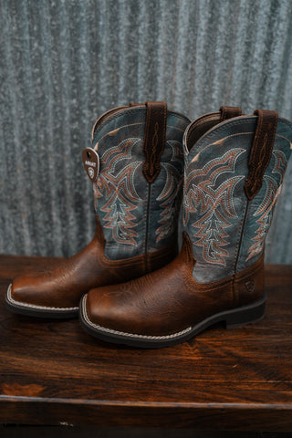 Pair of brown cowboy boots with intricate designs on a wooden surface and metal background