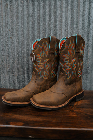 Pair of brown cowboy boots with intricate designs on a wooden surface and metal wall background