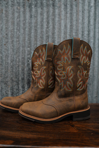 Pair of brown cowboy boots with intricate designs on a wooden surface and metal wall background