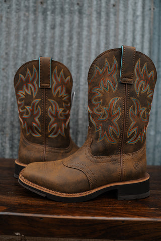Pair of brown cowboy boots with intricate designs on a wooden surface and metal wall background