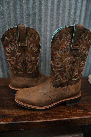 Pair of brown cowboy boots with flame pattern on a wooden surface and metal wall background