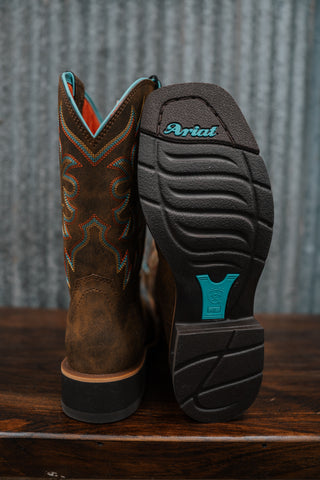 Brown cowboy boot with intricate design on a wooden surface, showing the Ariat logo.