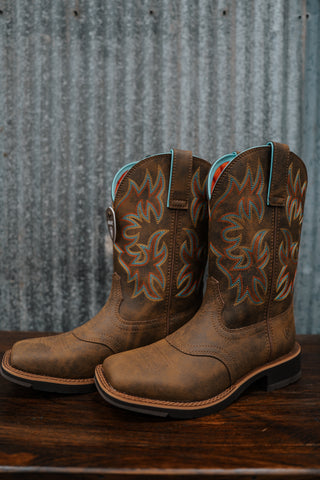 Pair of brown cowboy boots with turquoise accents on a wooden surface and metal wall background