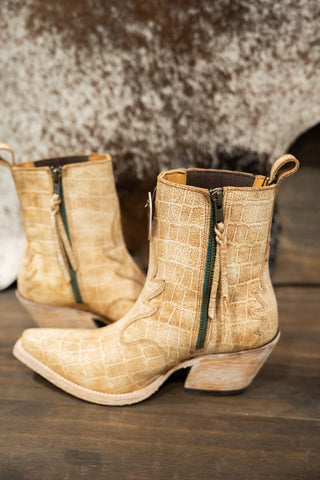 Beige crocodile-patterned boots with green zippers on a wooden surface.