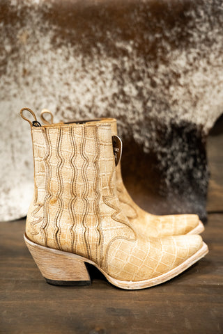 Pair of beige cowboy boots with a textured pattern on a wooden surface.